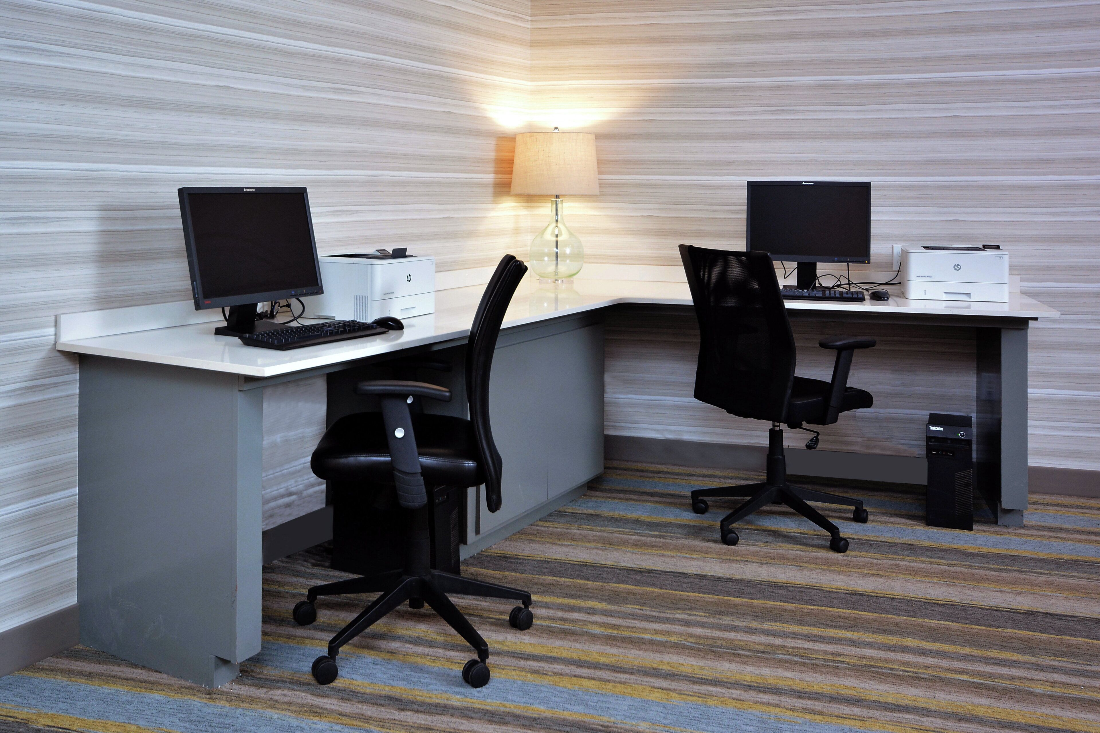 Habitación de hotel con dos escritorios, cada uno con una computadora, una silla e impresora.