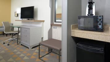 Une chambre d’hôtel équipée d’une télévision, d’un four à micro-ondes, d’une petite table, d’une chaise, d’un bureau et d’une poubelle.