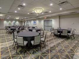 Un salón de conferencias con varias mesas y sillas, alfombra estampada e iluminación en el techo.