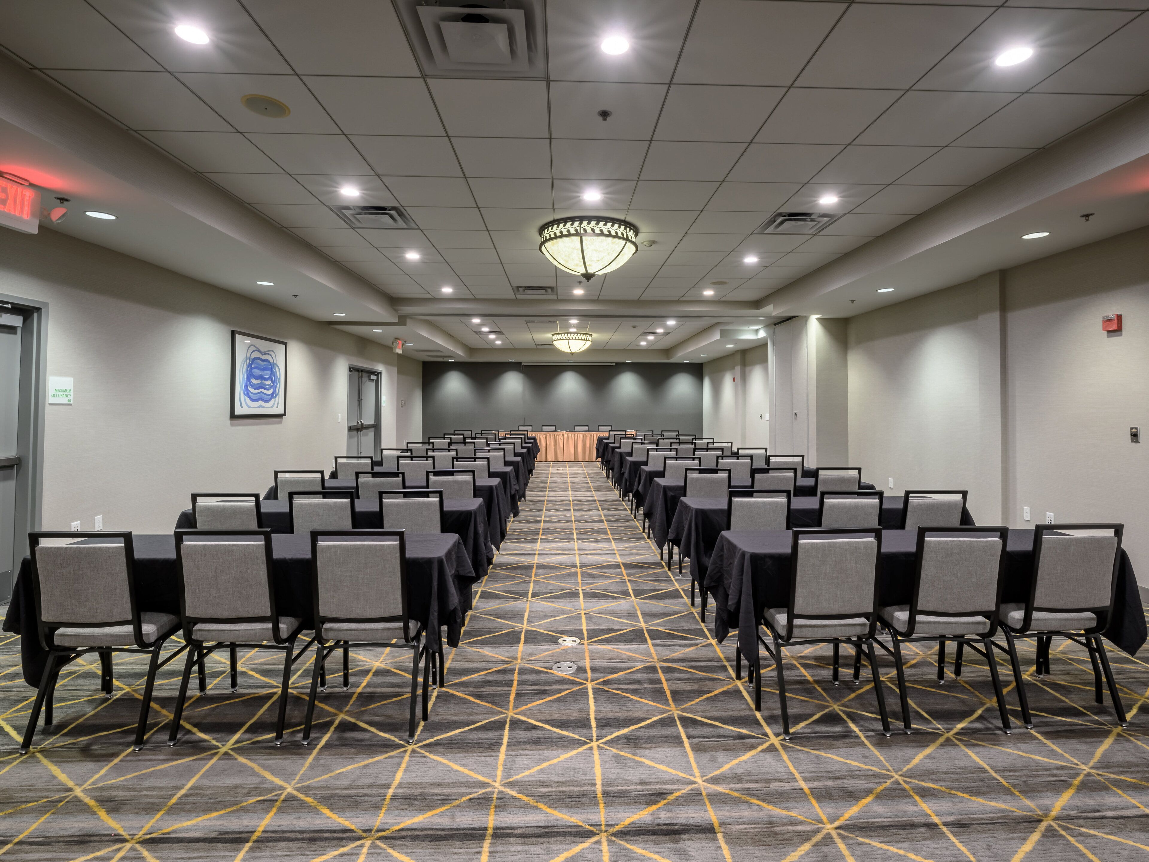 A conference room with rows of tables and chairs, a patterned carpet, and a chandelier.