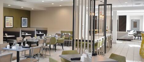 A modern dining area with tables and chairs, a decorative partition, and artwork on the walls.