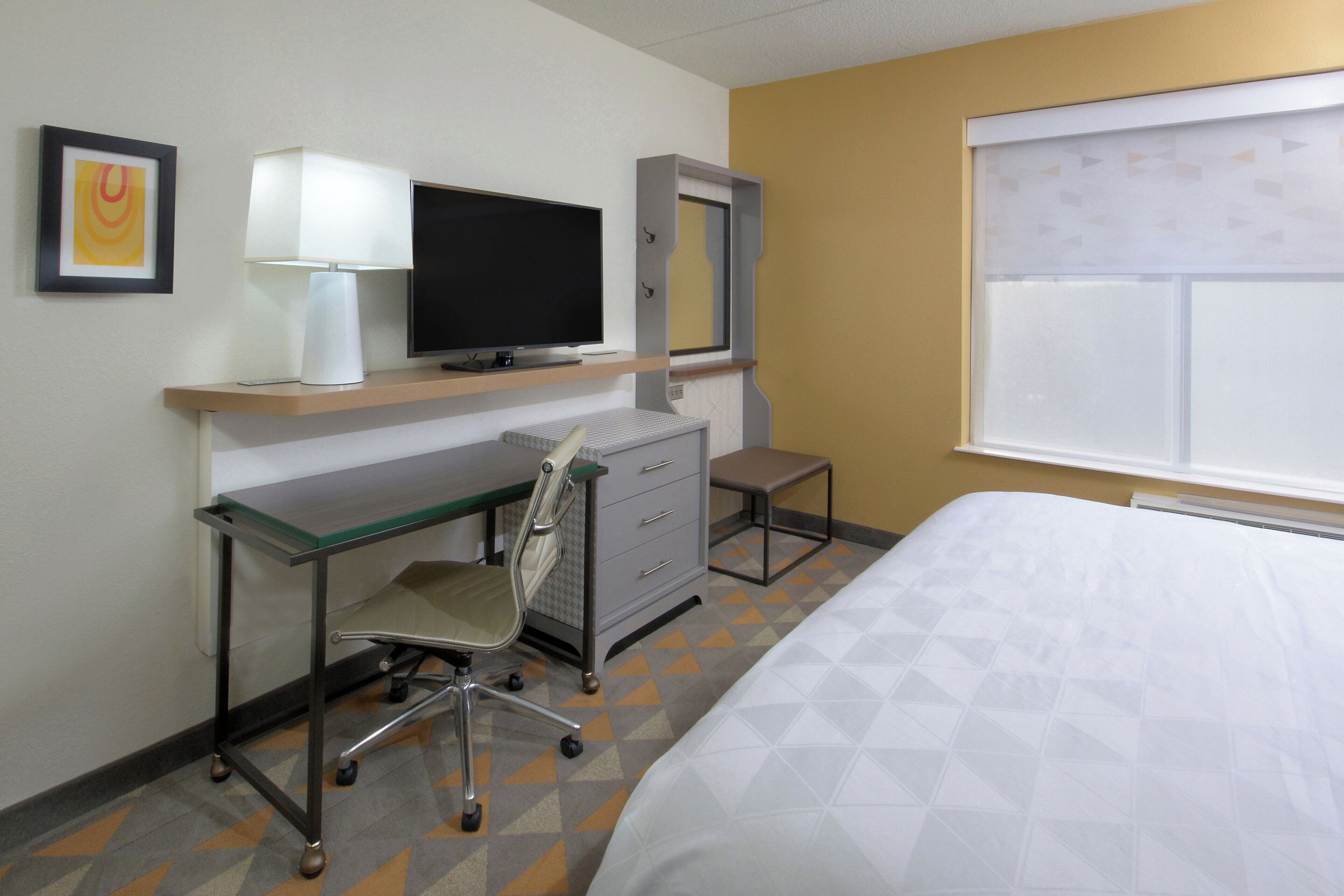 A hotel room with a bed, desk, chair, TV, and a window.