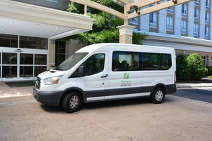 Una camioneta blanca estacionada frente a un edificio con un letrero de Holiday Inn, ventanas amplias y un acceso cubierto.