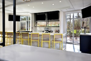 A modern bar area with a white countertop, yellow chairs, and a large window offering a view of trees.