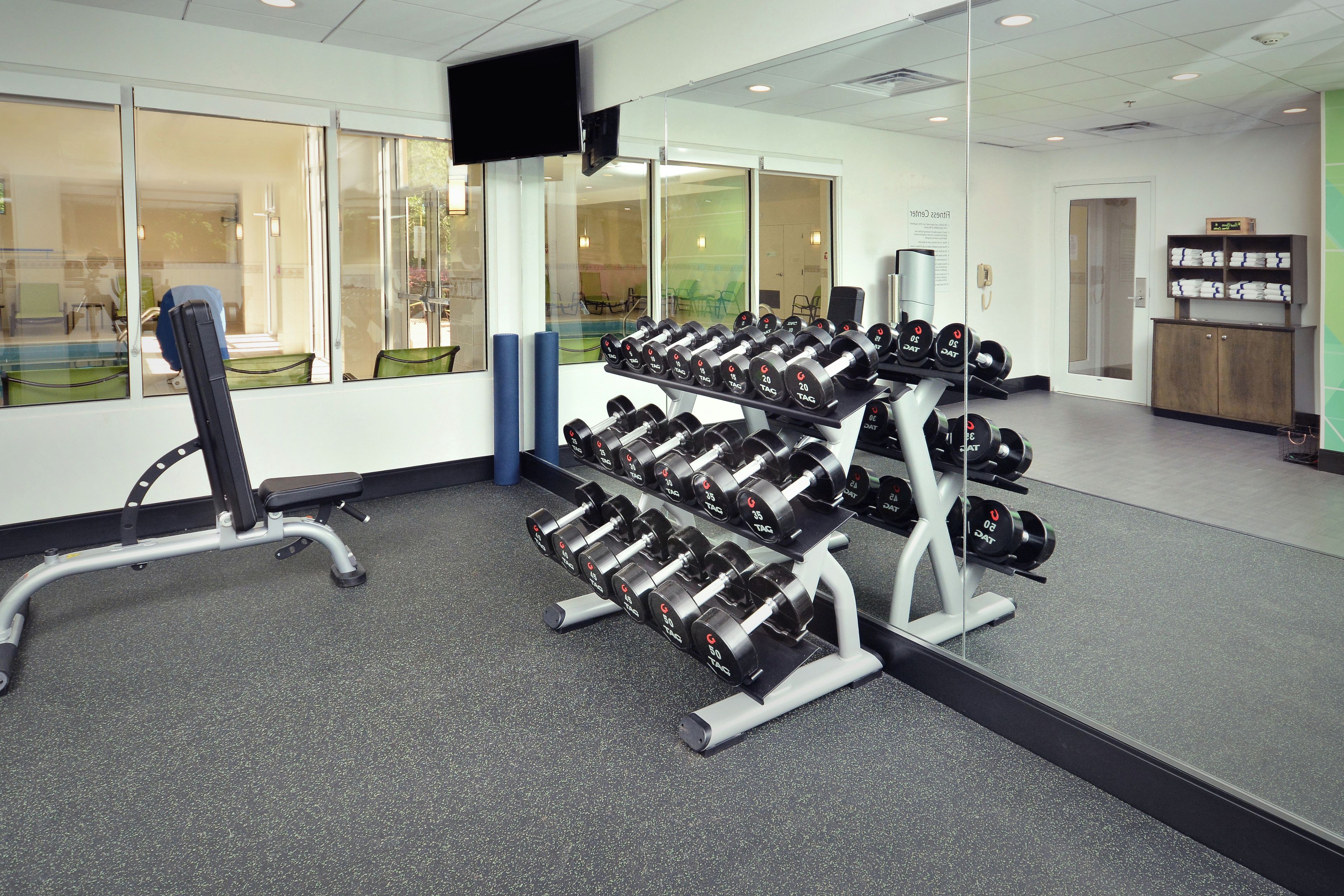 A gym with weightlifting equipment, a bench, and a television screen.