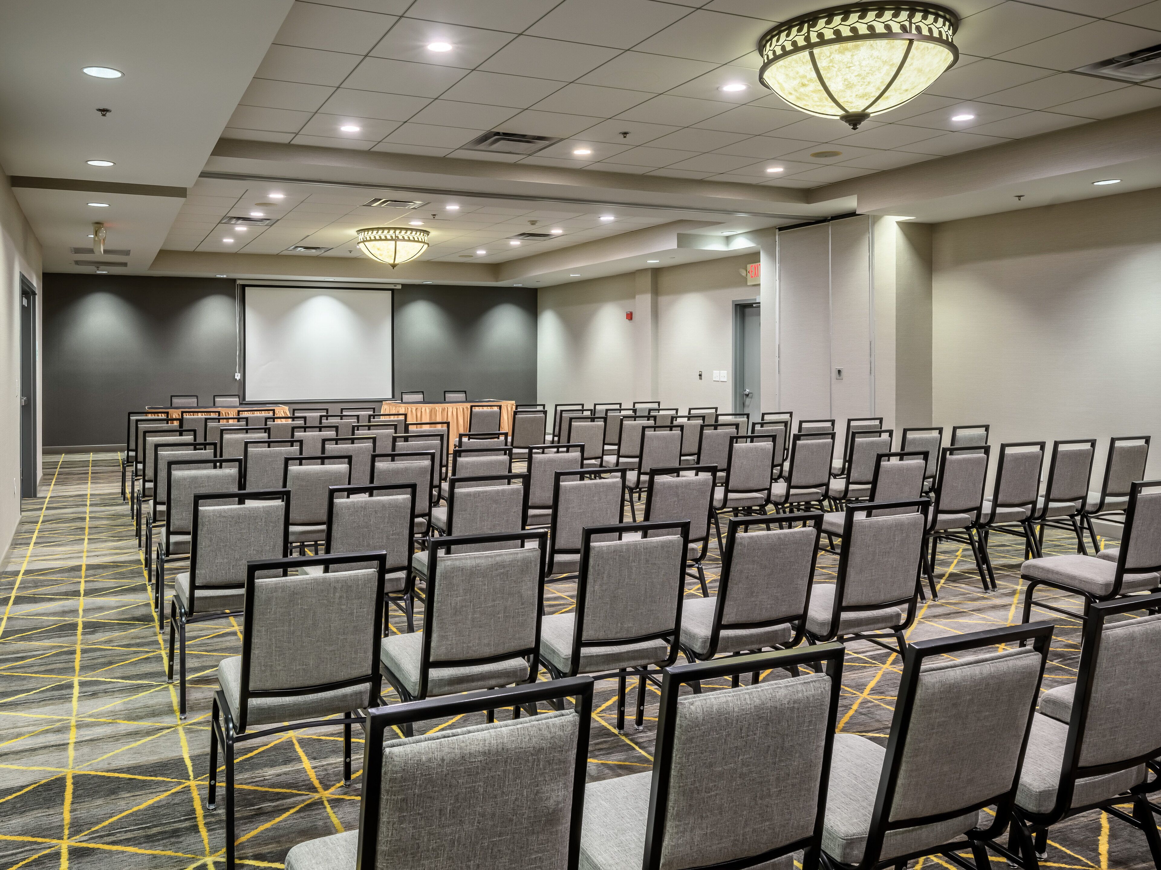 A conference room with rows of chairs, a projector screen, and a carpeted floor.