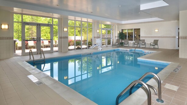 An indoor swimming pool with clear glass walls, a tiled floor, and a few lounge chairs outside. - Holiday Inn Raleigh-Durham Airport by IHG (Morrisville)