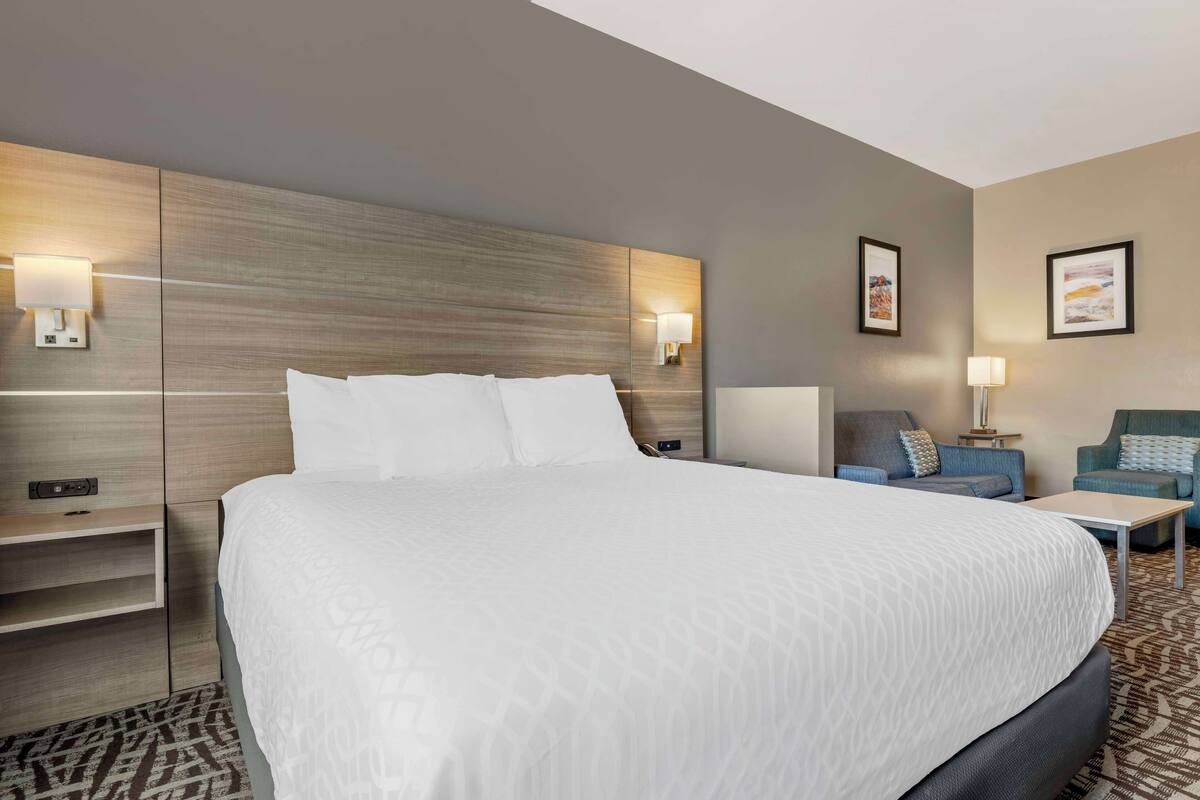 A hotel room with a large bed, a nightstand, a desk, a sofa, and two wall-mounted lamps.