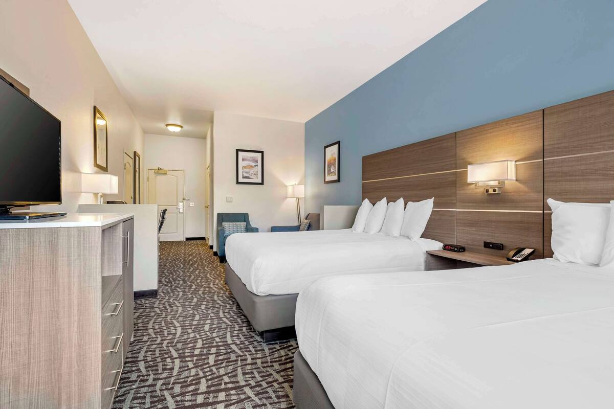 A hotel room with two beds, a desk, a TV, and a bathroom visible in the background.