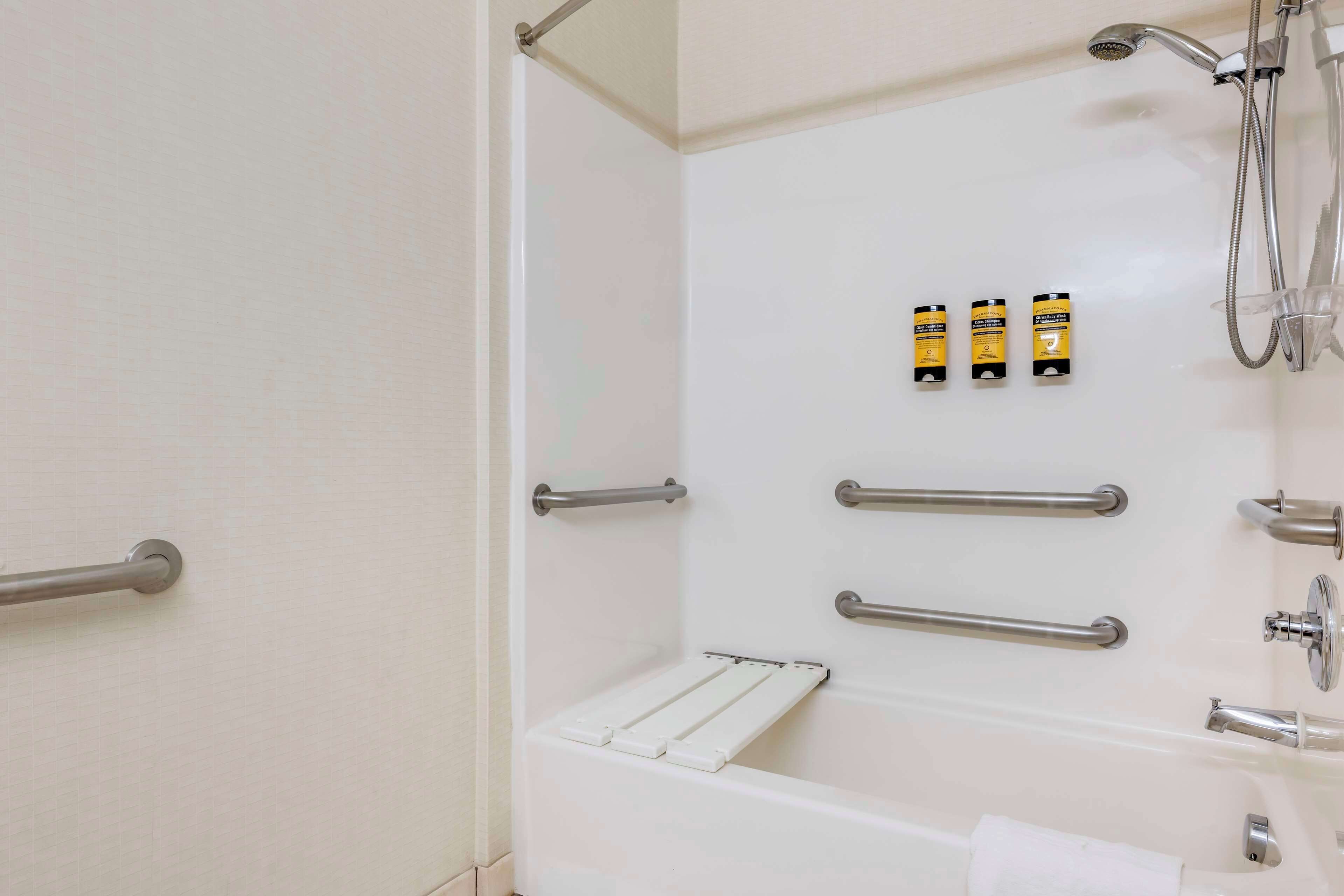 Ein Badezimmer mit einer weißen Wanne, Haltegriffen, einer Duschbrause und zwei Shampoo-Flaschen.