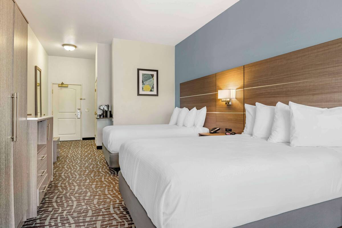 A hotel room with two beds, a wardrobe, a mirror, a framed picture, and a bedside lamp.