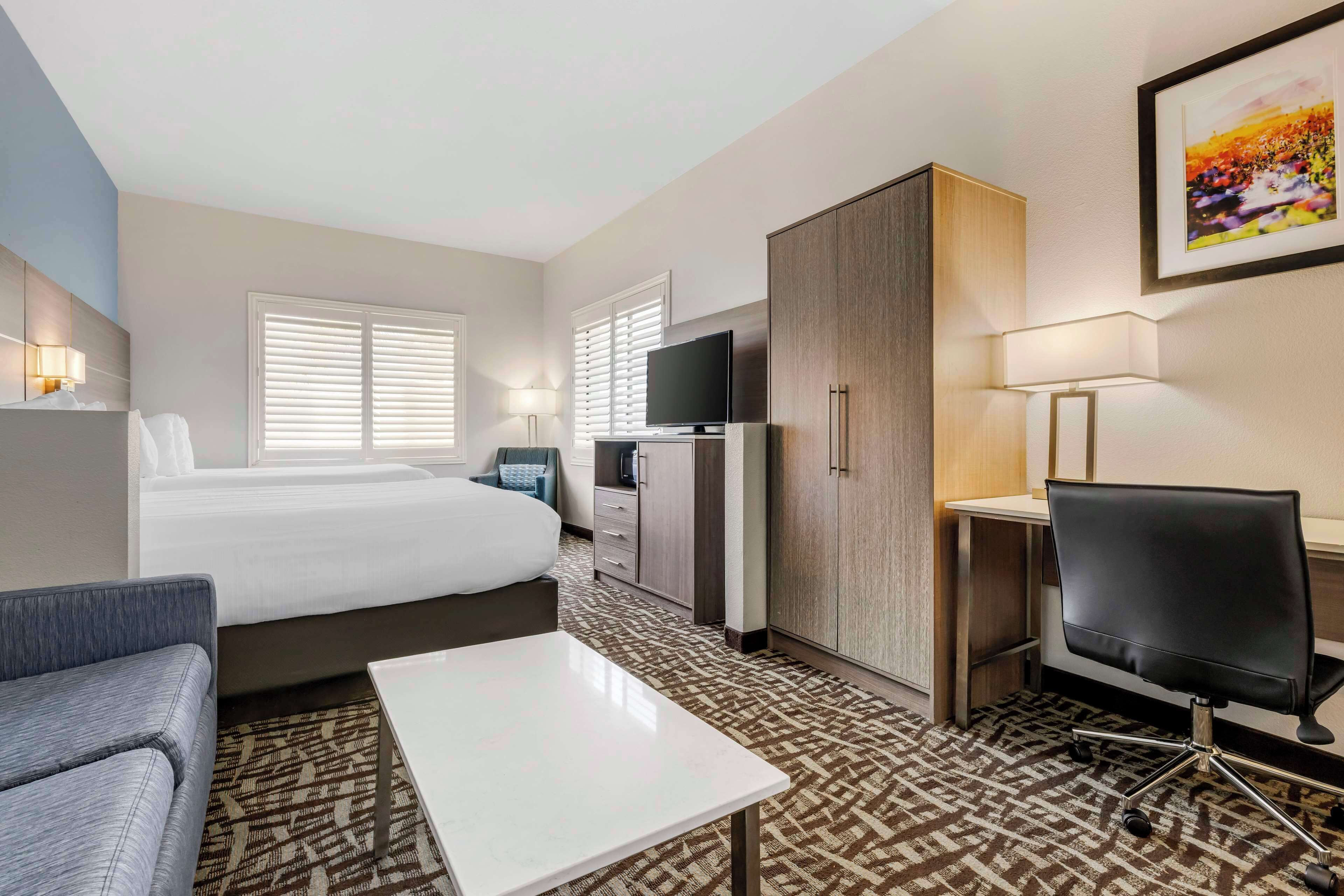 A hotel room with a bed, a desk, a chair, a TV, and a wardrobe.
