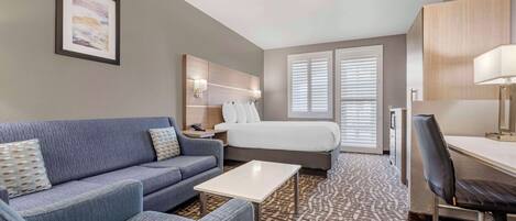 A hotel room with a sofa, a bed, a desk, and a patterned carpet.