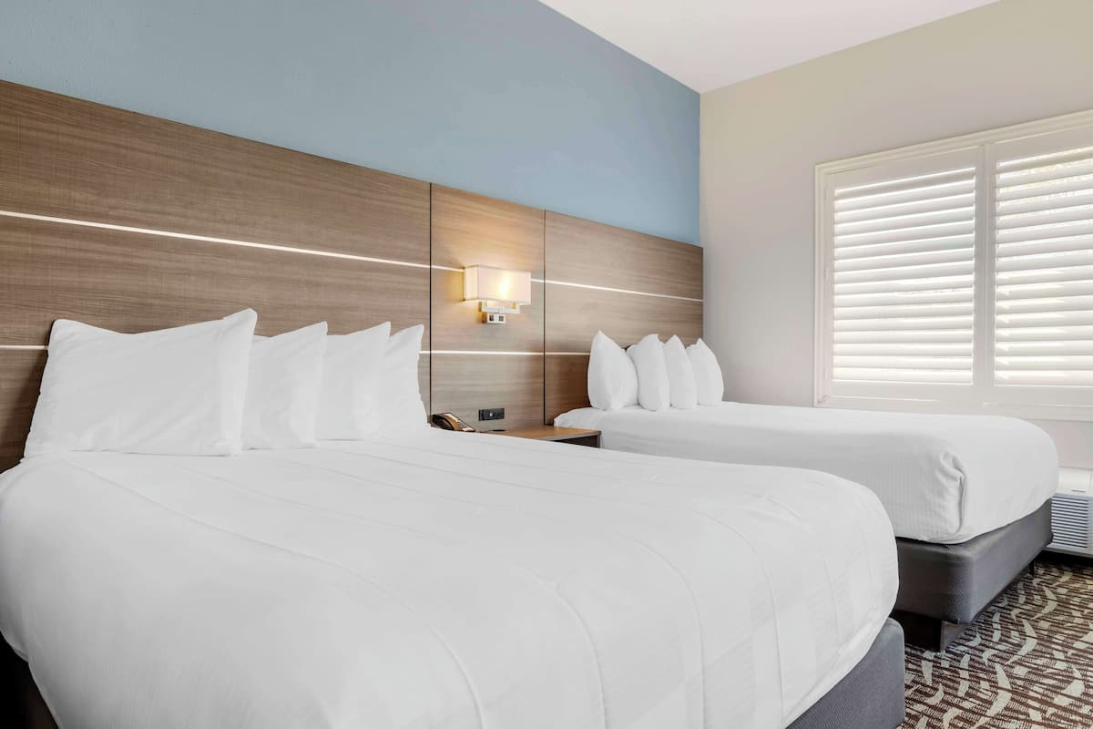 A hotel room with two beds, a wooden headboard, a nightstand, and a window with blinds.
