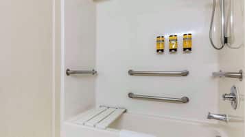 A modern bathroom with a bathtub, grab bars, a towel rack, and three bottles of shampoo.