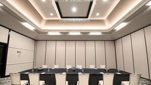 Un salón de conferencias con una larga mesa, sillas blancas y una araña.