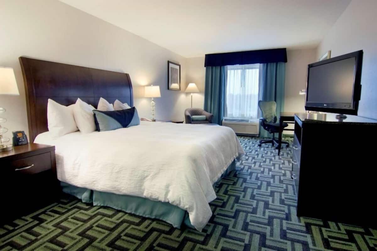 A hotel room with a large bed, a desk with a computer, a TV, and a chair.