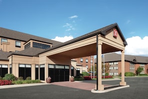 A hotel with a covered entrance, multiple windows, and a brick building in the background. - Hilton Garden Inn South Bend (South Bend)