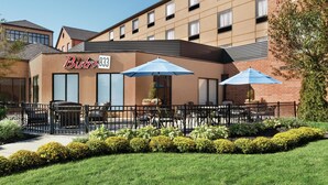 Exterior de un hotel con un letrero que dice "Bistro 933", mesas al aire libre con sombrillas y un jardín bien cuidado.