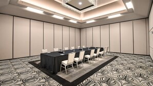 Un salón de conferencias con una larga mesa, sillas blancas, una alfombra estampada y un candelabro.