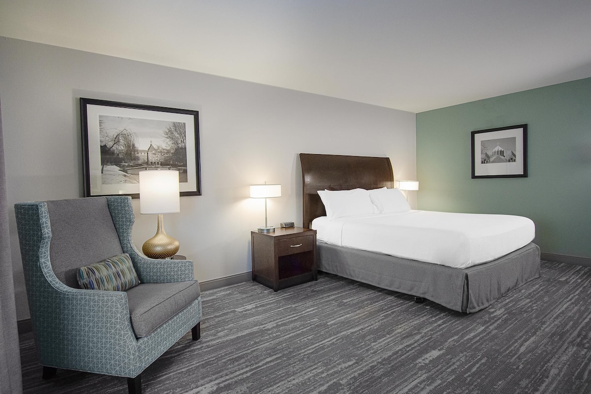 A hotel room with a bed, a chair, two nightstands with lamps, and two framed pictures on the walls.