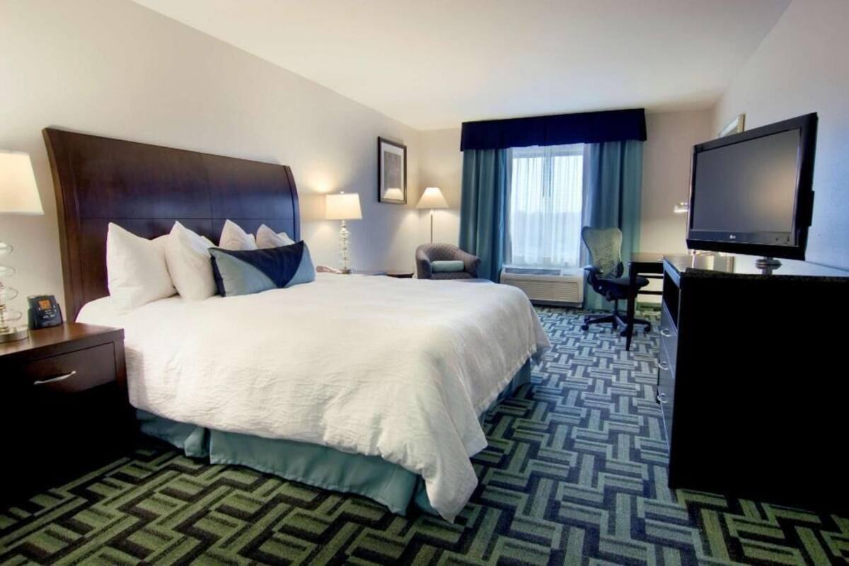 A hotel room with a large bed, a desk with a computer, a TV, and a chair.