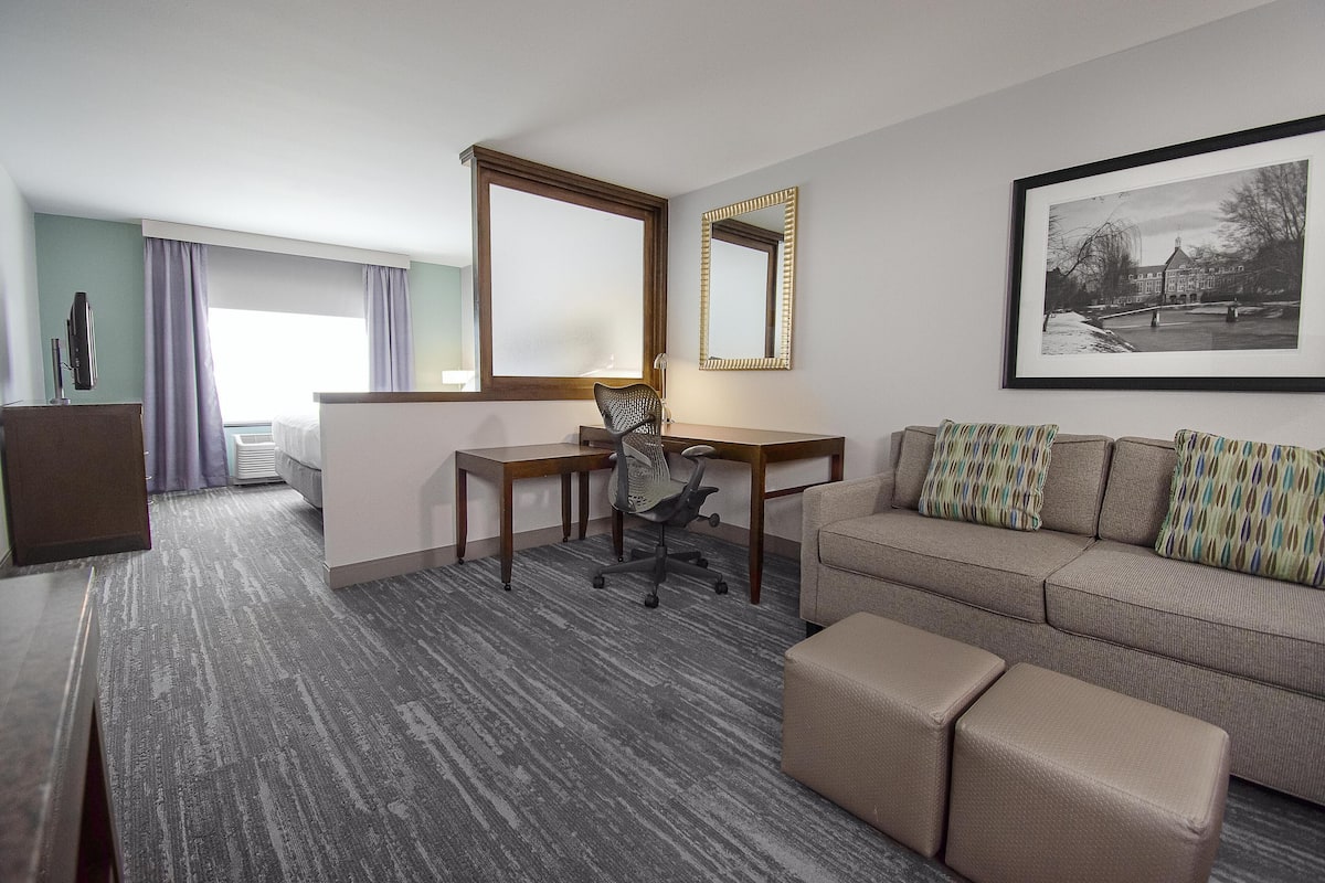 A hotel room with a desk, office chair, sofa, and ottoman.