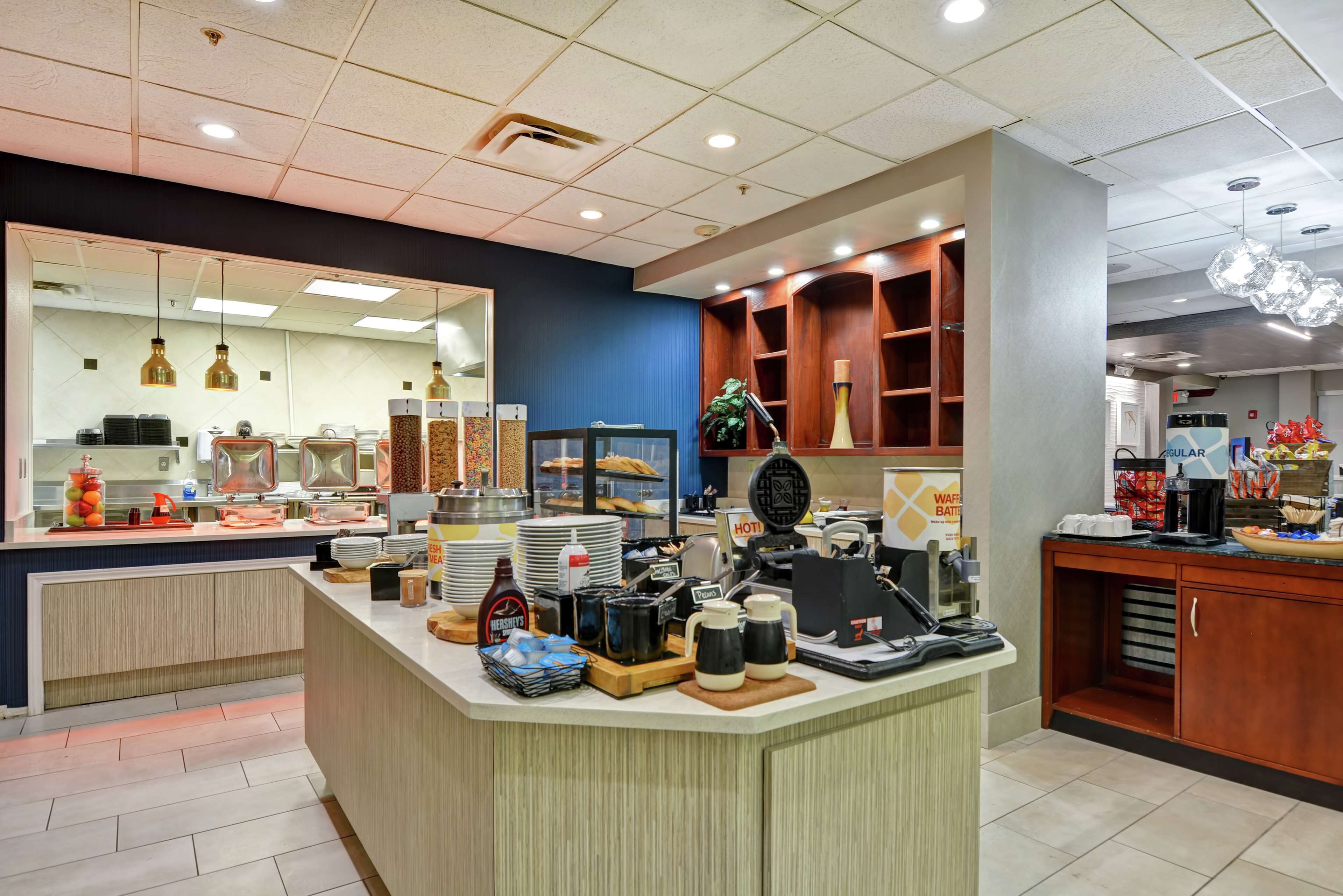 A breakfast bar with a variety of food items, a coffee station, and a mirror reflecting the kitchen area.
