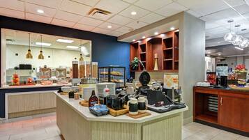 A breakfast bar with a variety of food items, a coffee station, and a mirror reflecting the kitchen area.