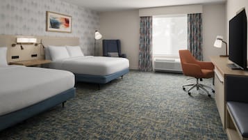 A hotel room with two beds, a desk with a television, a chair, and a window with curtains.