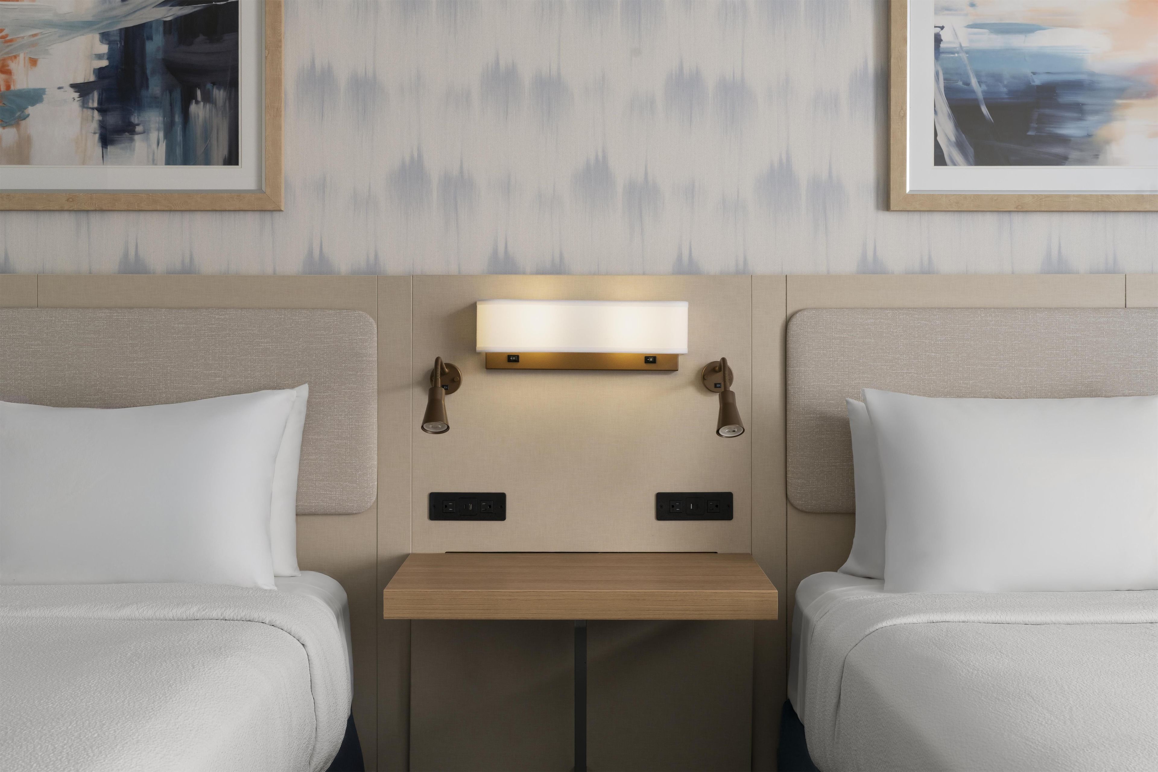 Habitación de hotel con dos camas, una mesita de noche y una lámpara fijada en la pared.