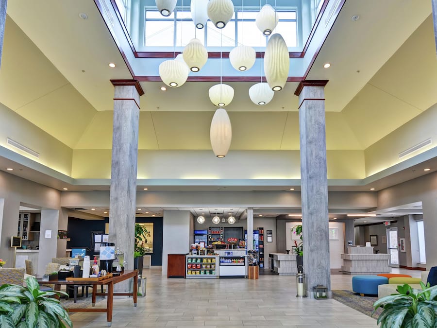A spacious lobby with a high ceiling, large columns, and a central seating area with a counter and vending machines.