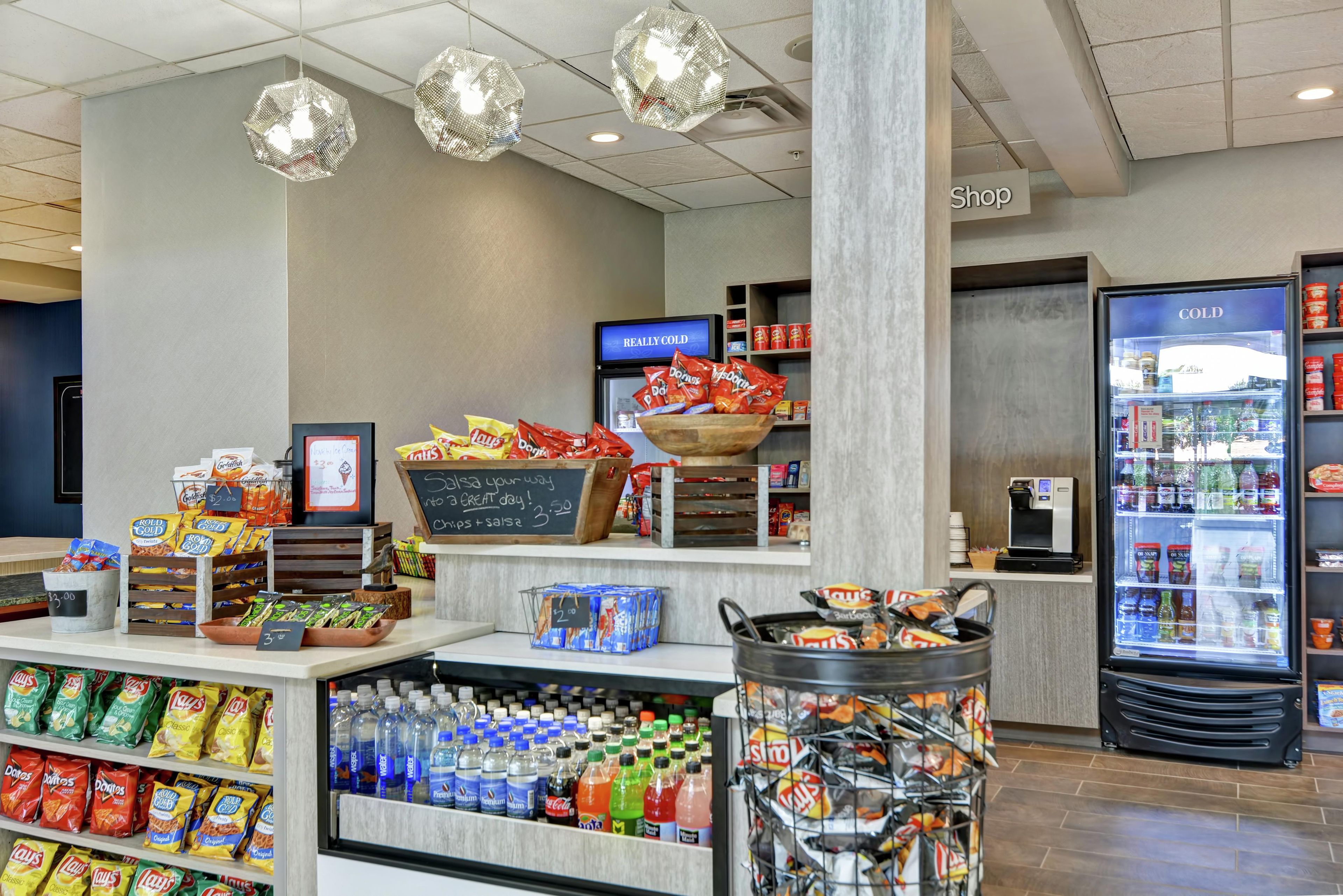 Een afdeling met snacks en drankjes in een winkel, met verschillende soorten chips, flessen water en een koelkast voor koude drank.