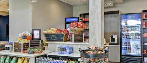 Una sección de snacks y bebidas en una tienda con papas fritas, agua embotellada y un refrigerador para bebidas frías.