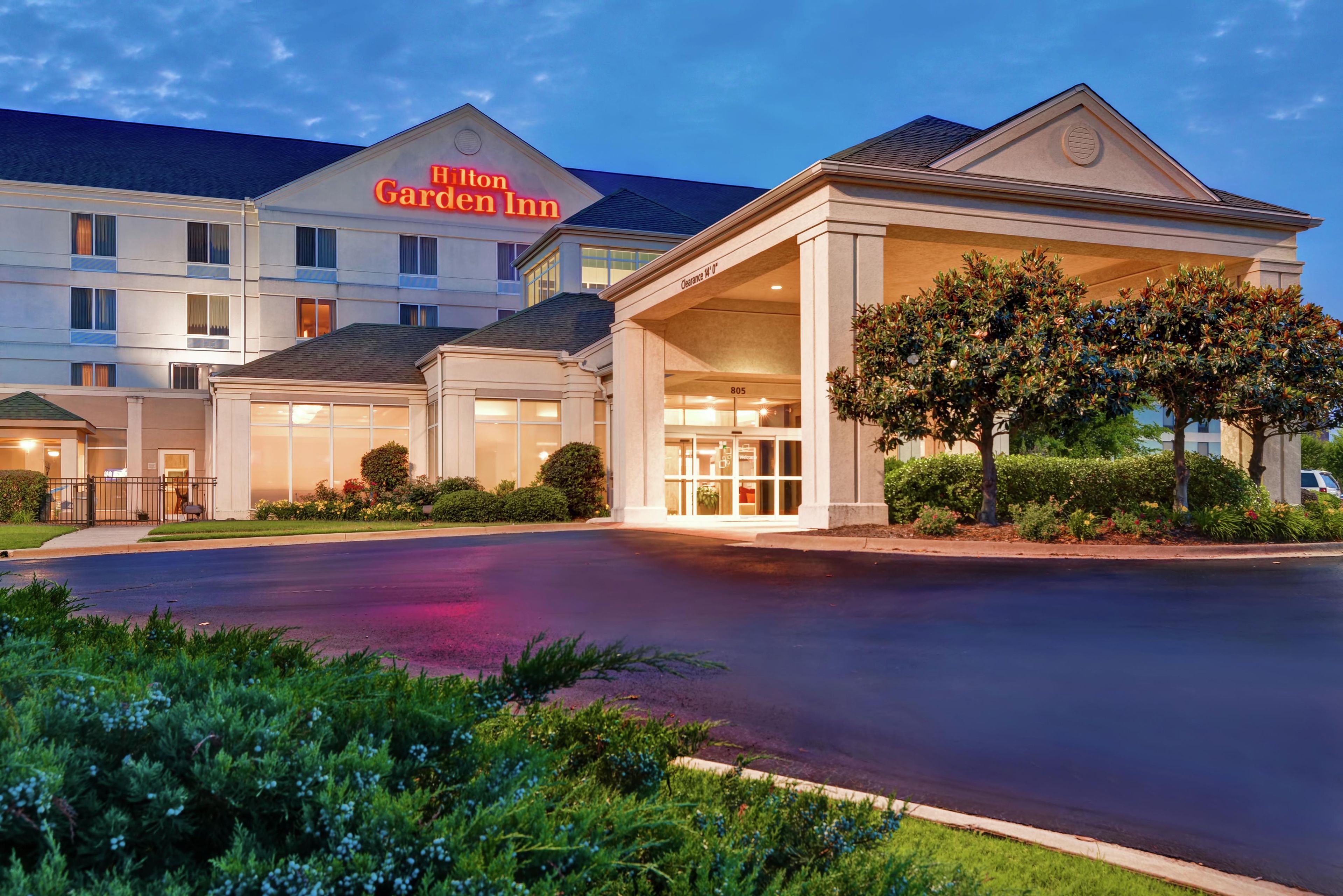 Un Hilton Garden Inn con entrada despejada, una zona de espera cubierta y un césped bien cuidado.