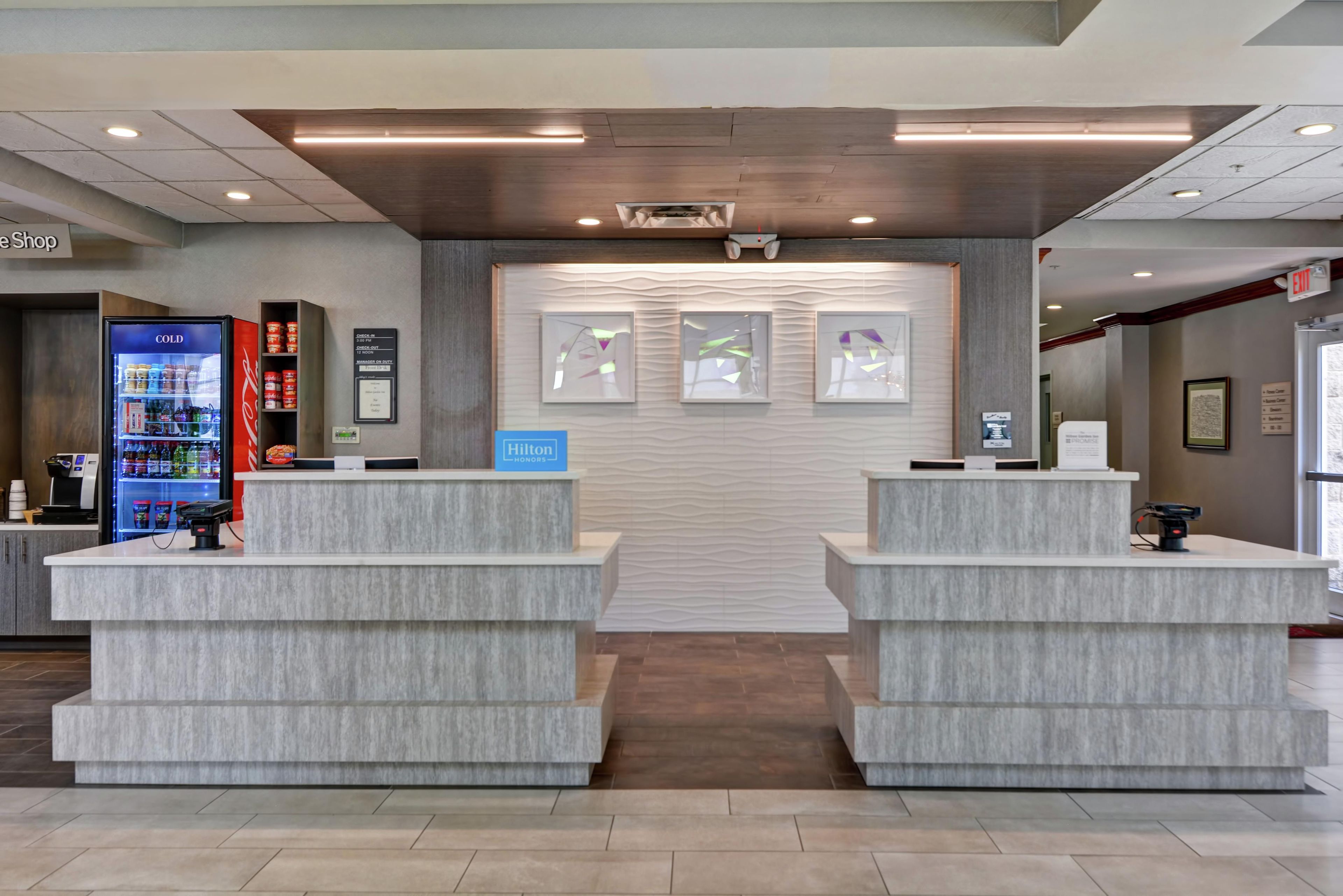 A hotel reception area with a modern design, featuring two reception desks, a vending machine, and a wall-mounted information board.