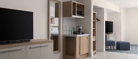 Una habitación de hotel moderna con televisor de pantalla plana, kitchenette, zona de estar y un espejo grande.