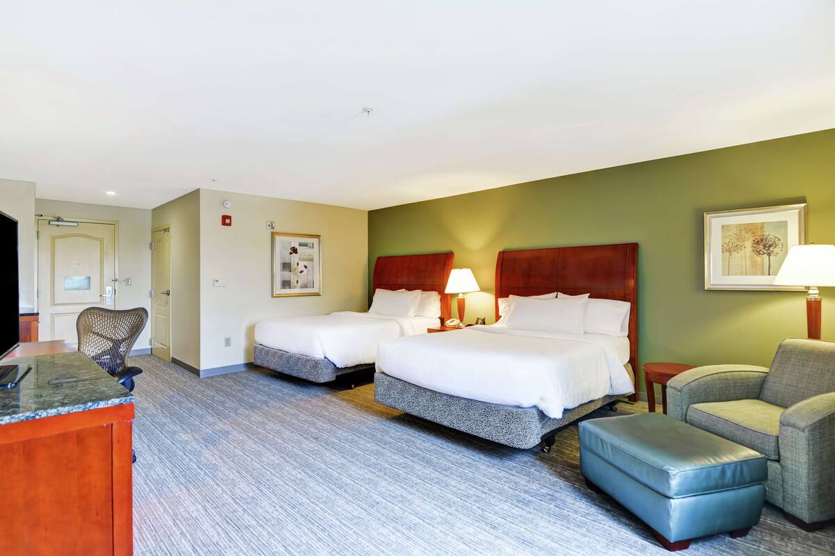 Ein Hotelzimmer mit zwei Betten, einem Schreibtisch, einem Stuhl und einem kleinen Hocker.