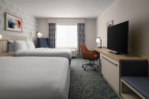 A hotel room with two beds, a desk, a television, and a chair.