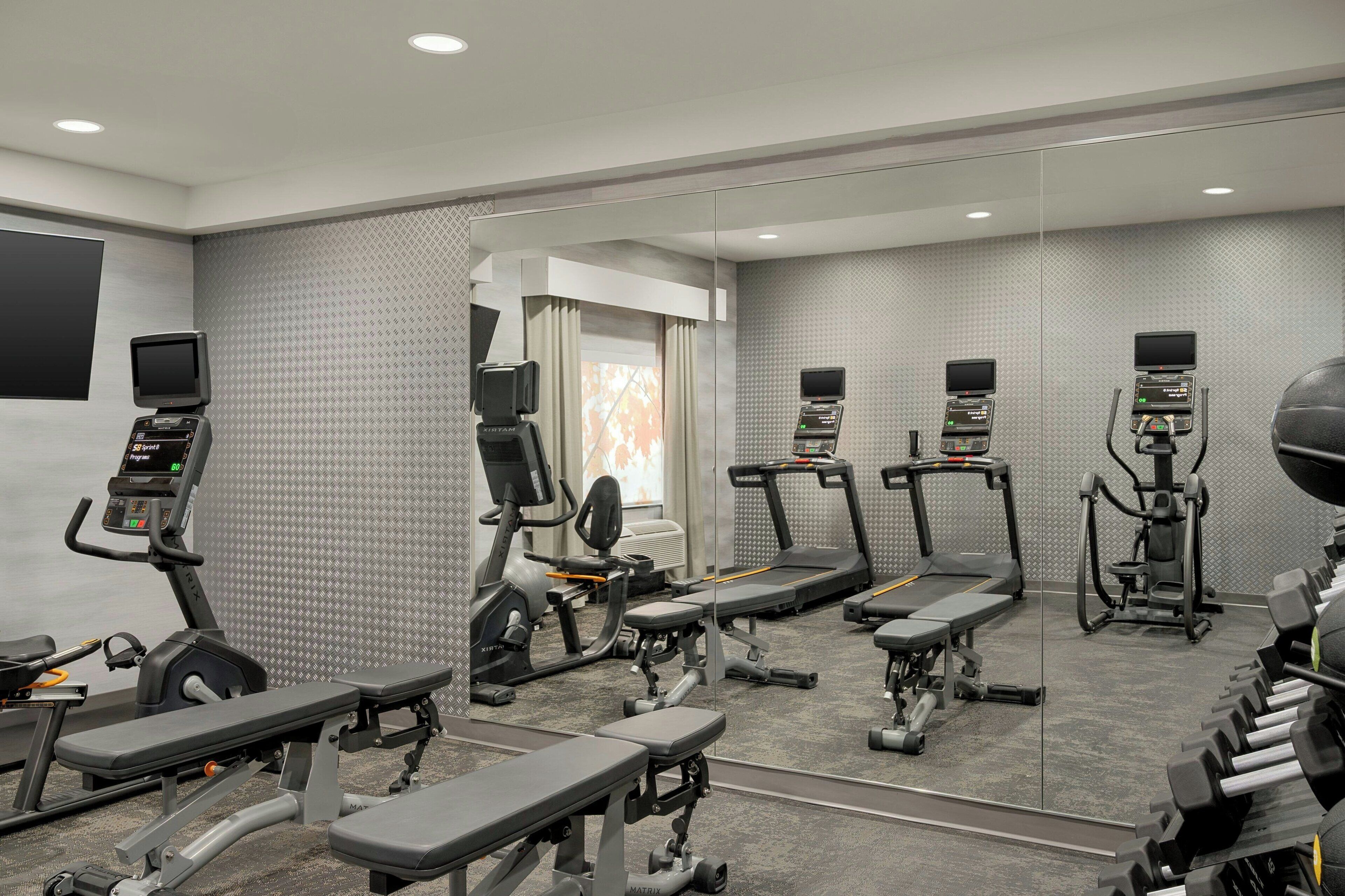 Une salle de sport moderne équipée de divers appareils d’exercice, notamment des tapis de course, des vélos elliptiques et des poids libres.