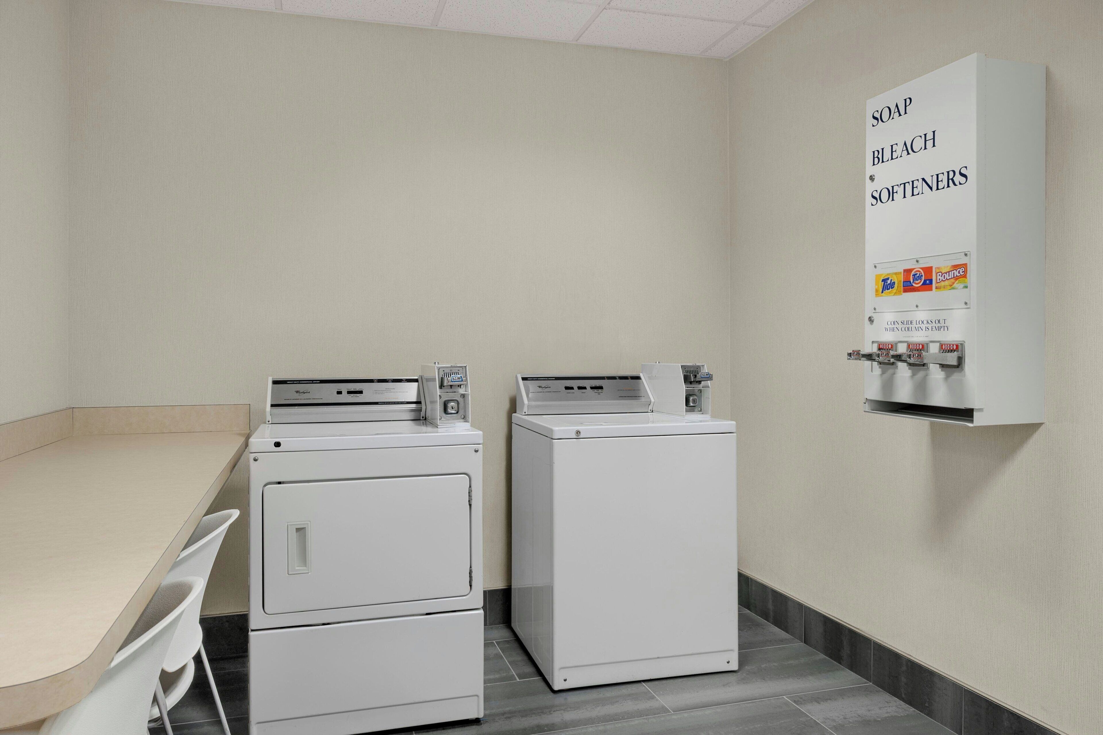 Une buanderie équipée de deux machines à laver, d’un sèche-linge et d’un distributeur de savon et de lessive fixé au mur.
