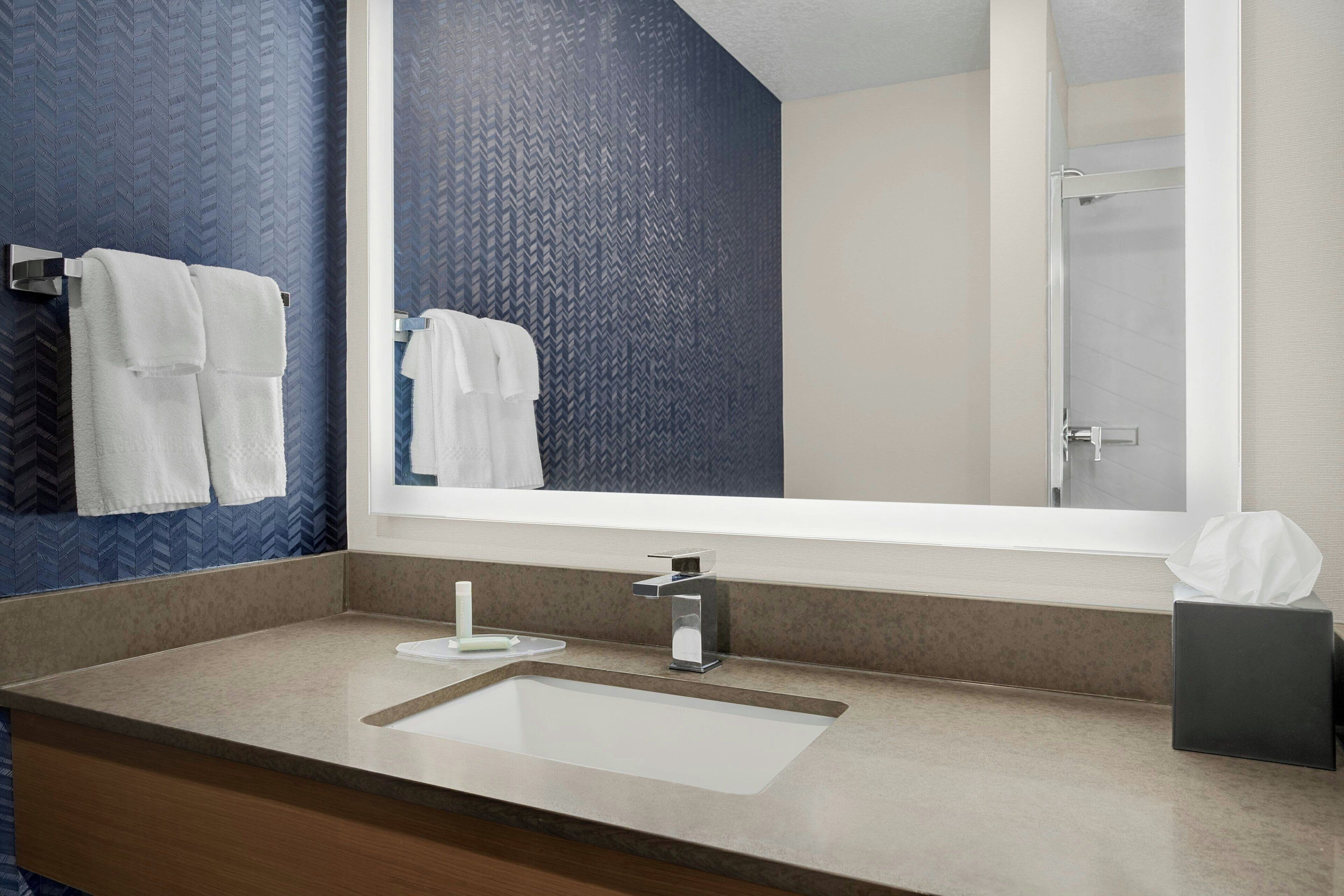 A bathroom with a large mirror, a sink, and towels on the wall.