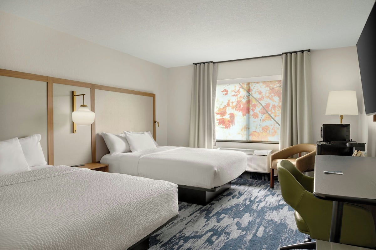 A hotel room with two beds, a desk, a chair, a television, and a window with curtains.