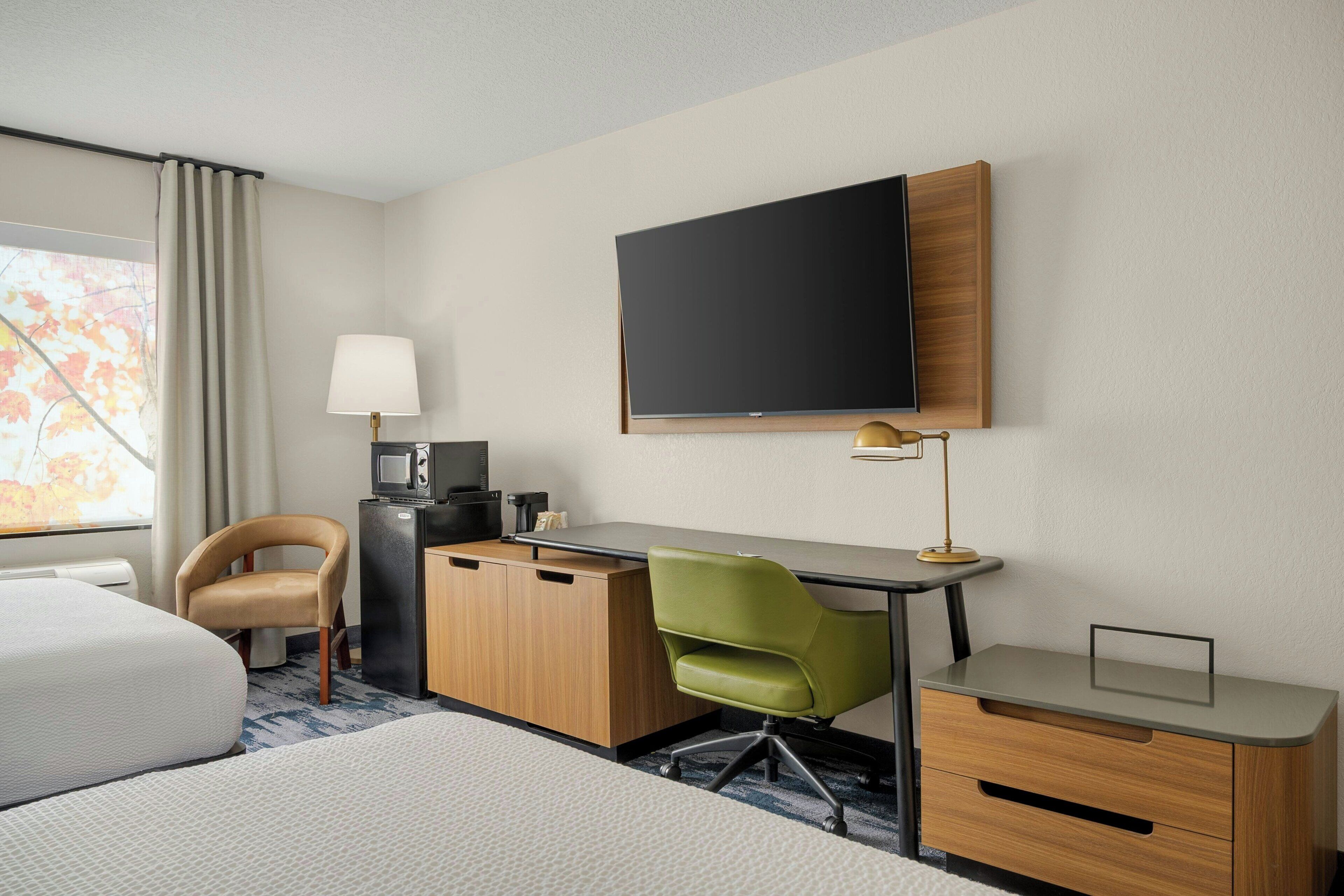 Una habitación de hotel con una cama, un escritorio con computadora, televisión y una silla.