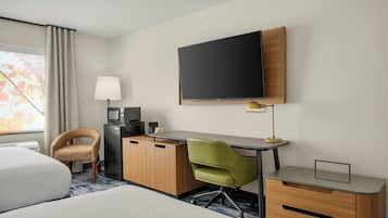 Una habitación de hotel con una cama, un escritorio con computadora, televisión y una silla.