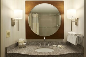 A bathroom with a round mirror, two wall-mounted lights, a sink with toiletries, and a towel rack.