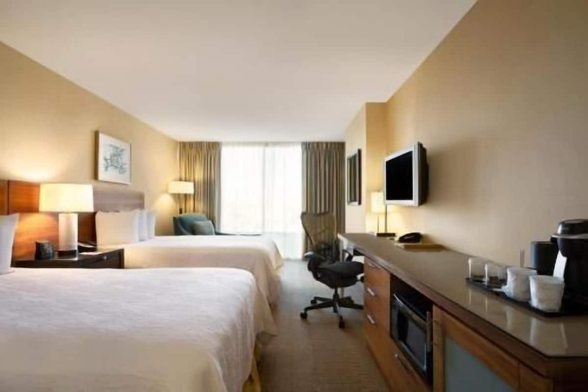 A hotel room with two beds, a desk with a flat-screen TV, a chair, and a coffee maker.