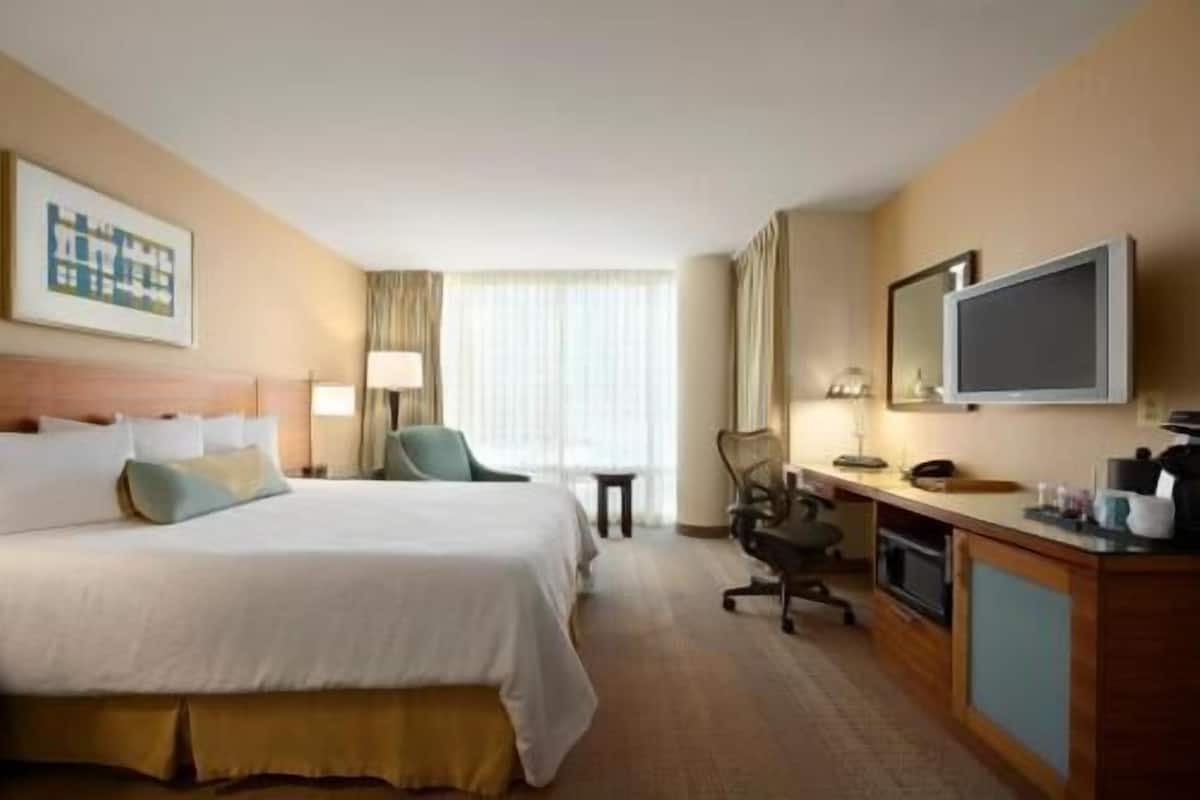 A hotel room with a bed, desk, chair, TV, and a window with curtains.