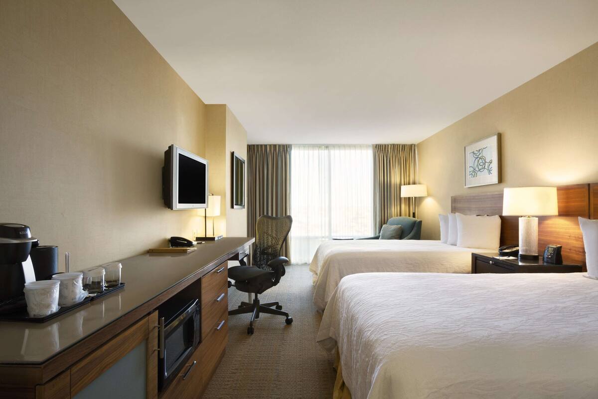 A hotel room with two beds, a desk with a coffee maker, a TV, and a chair.