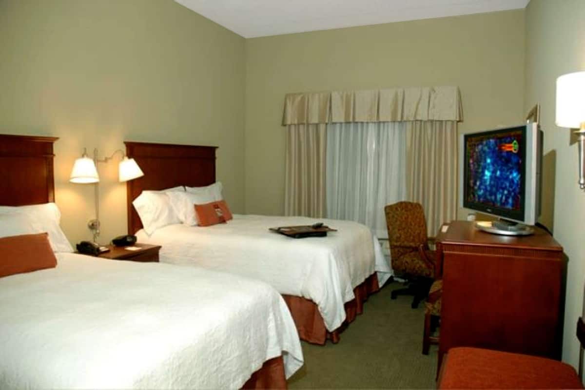 A hotel room with two beds, a television, a chair, and a desk.